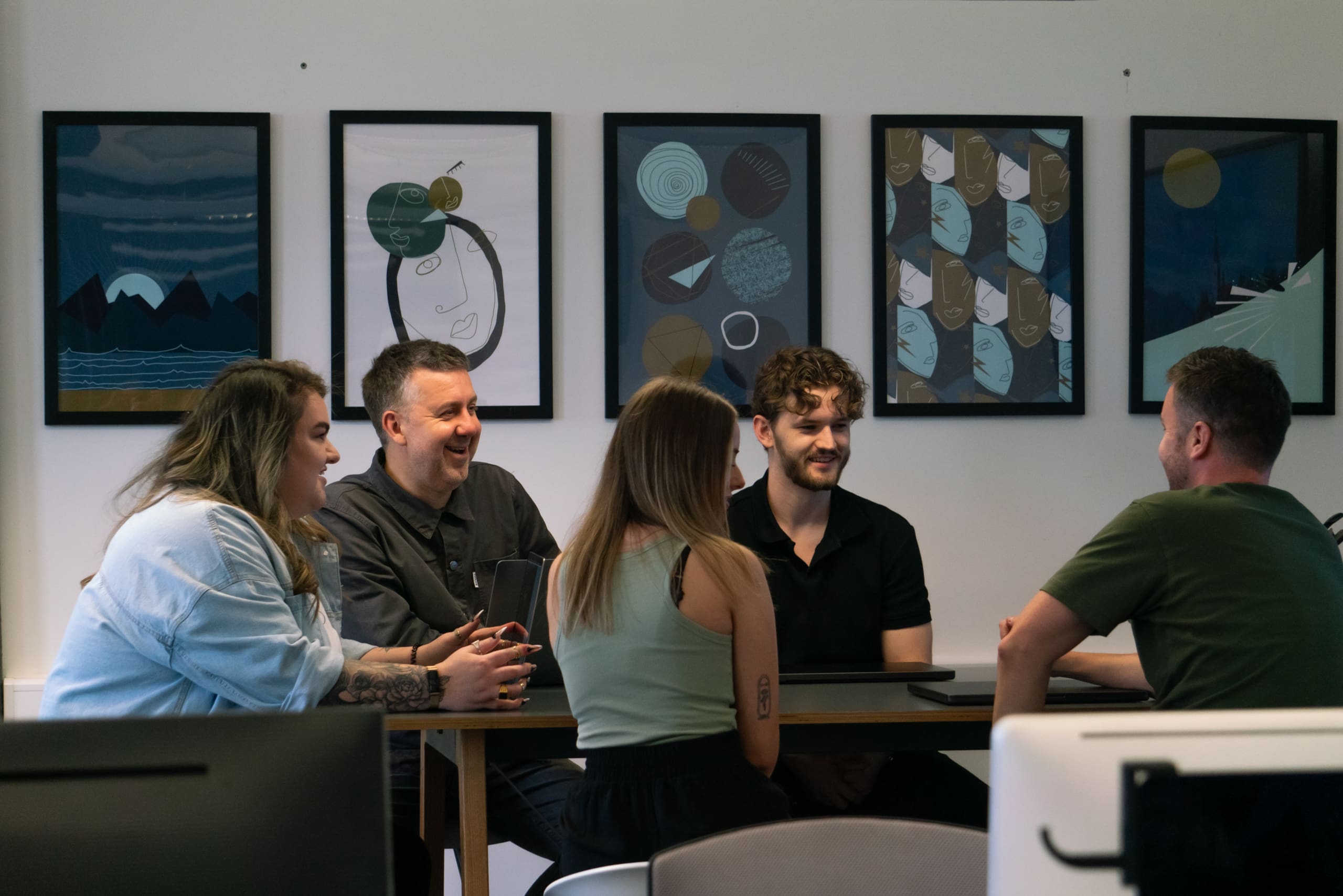 A photo of the team sat on a table having a meeting and discussing projects.