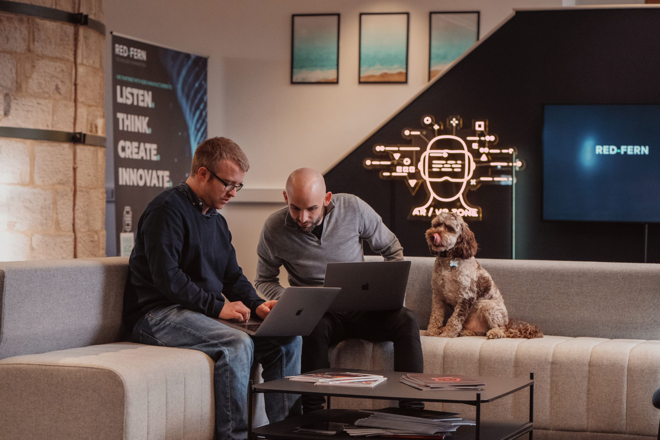 A photo of our MD Alex Heeney, sittin giwth Adam Wilson, both with laptops on their knees and Cockapoo Walter sat on the sofa beside them